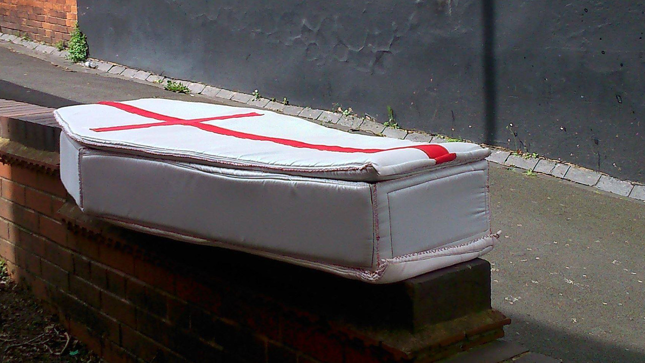 Soft sculpture called Coffin on a wall. Coffin has a St. George's Cross on the top.