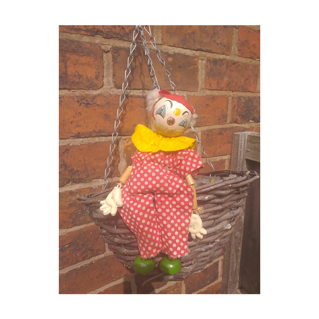 Vintage clown puppet in hanging basket in yard in the sunshine