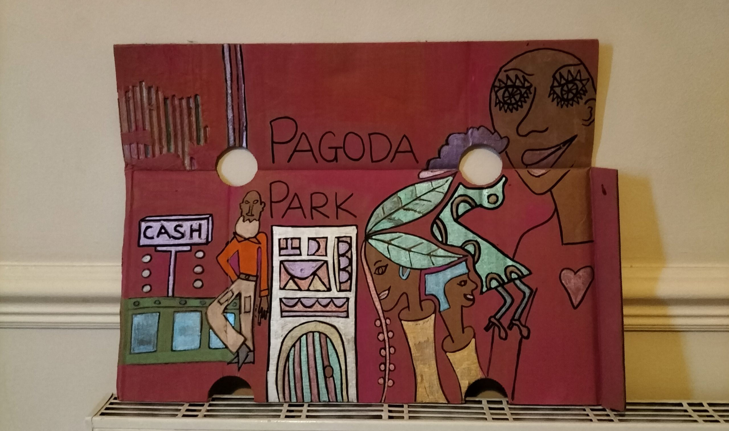 Cardboard art - Pagoda Park - a night club from 1980s Birmingham, UK. Man at cash desk, words Pagoda Park on the piece. People images mixed in with leaves for hair and around a hole in the piece where the hole is empty and where a face would have been. Woman to the right of the work with a heart on her top.