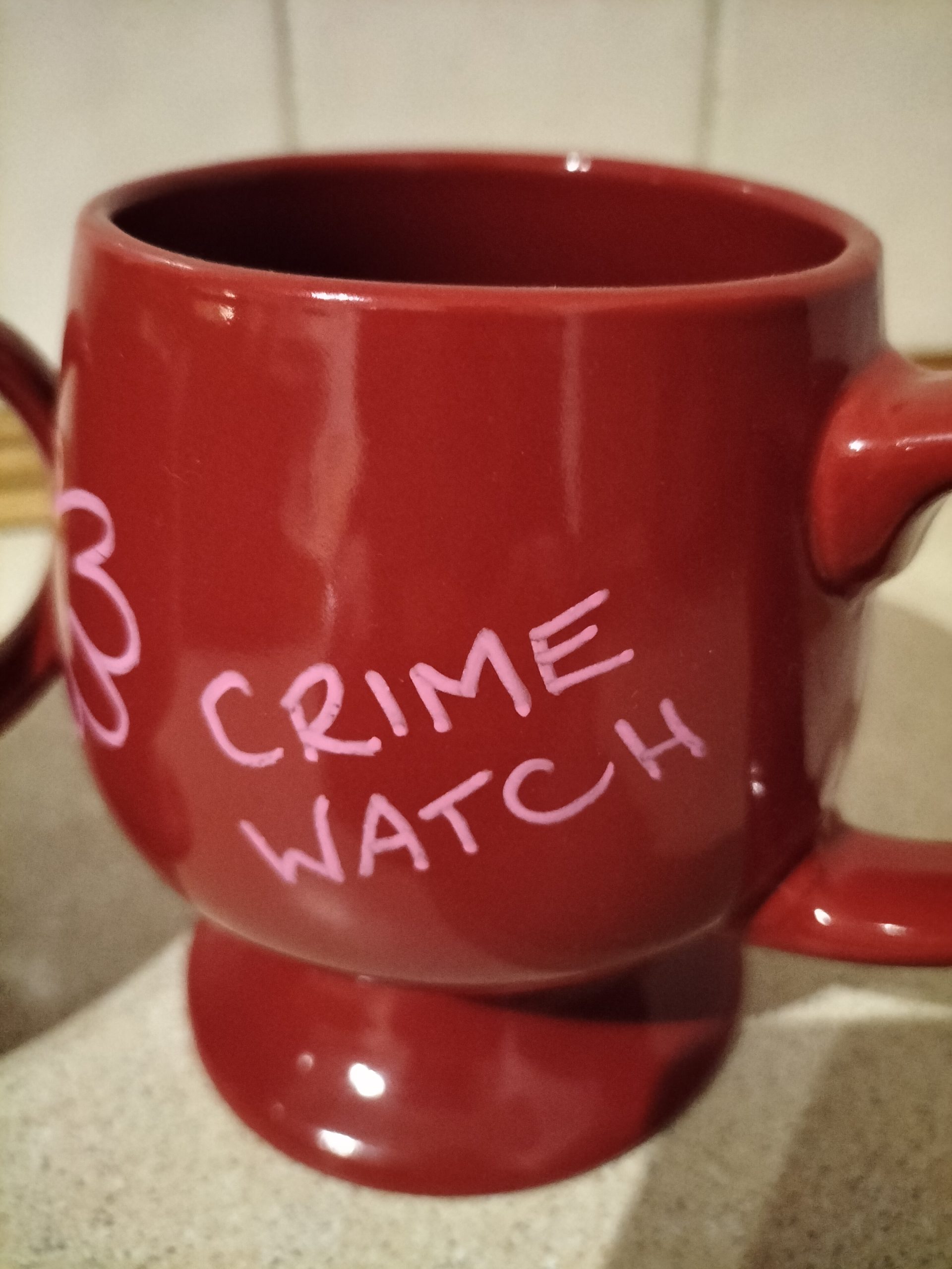 Pair of mugs called Crime Watch. Burgundy, thick heavy mugs with illustration on both mugs. Foot standing on a wrist with a watch. Words - Crime Watch on one mug. No Love I don't think so appears on the mugs too. Image of two faces on one mug. All hand painted. Original one off art work. Like little goblets with handles.