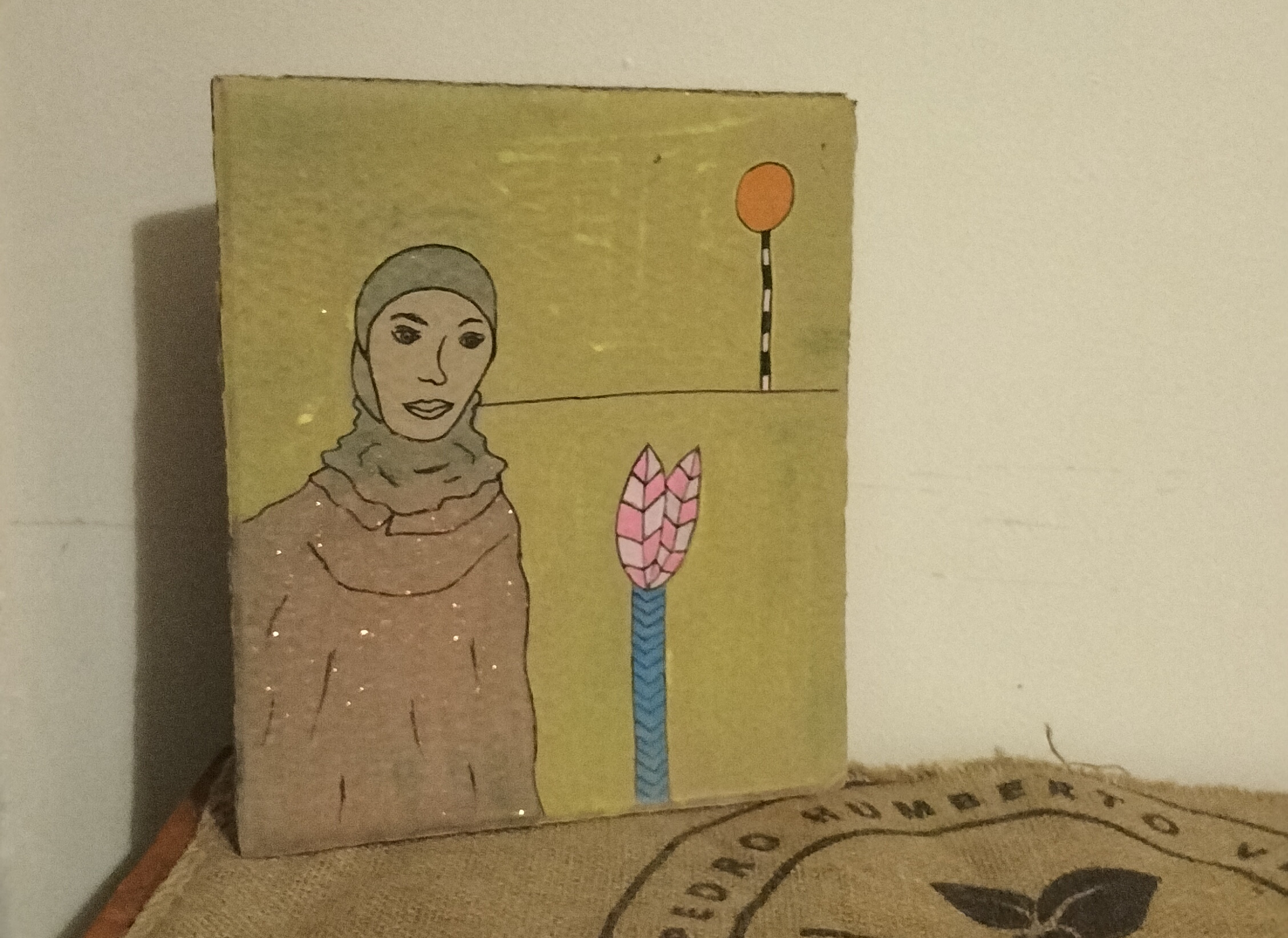 Muslim woman cardboard art. Woman on left of art work and plant and pelican crossing light on the right of the image. Yellow background.