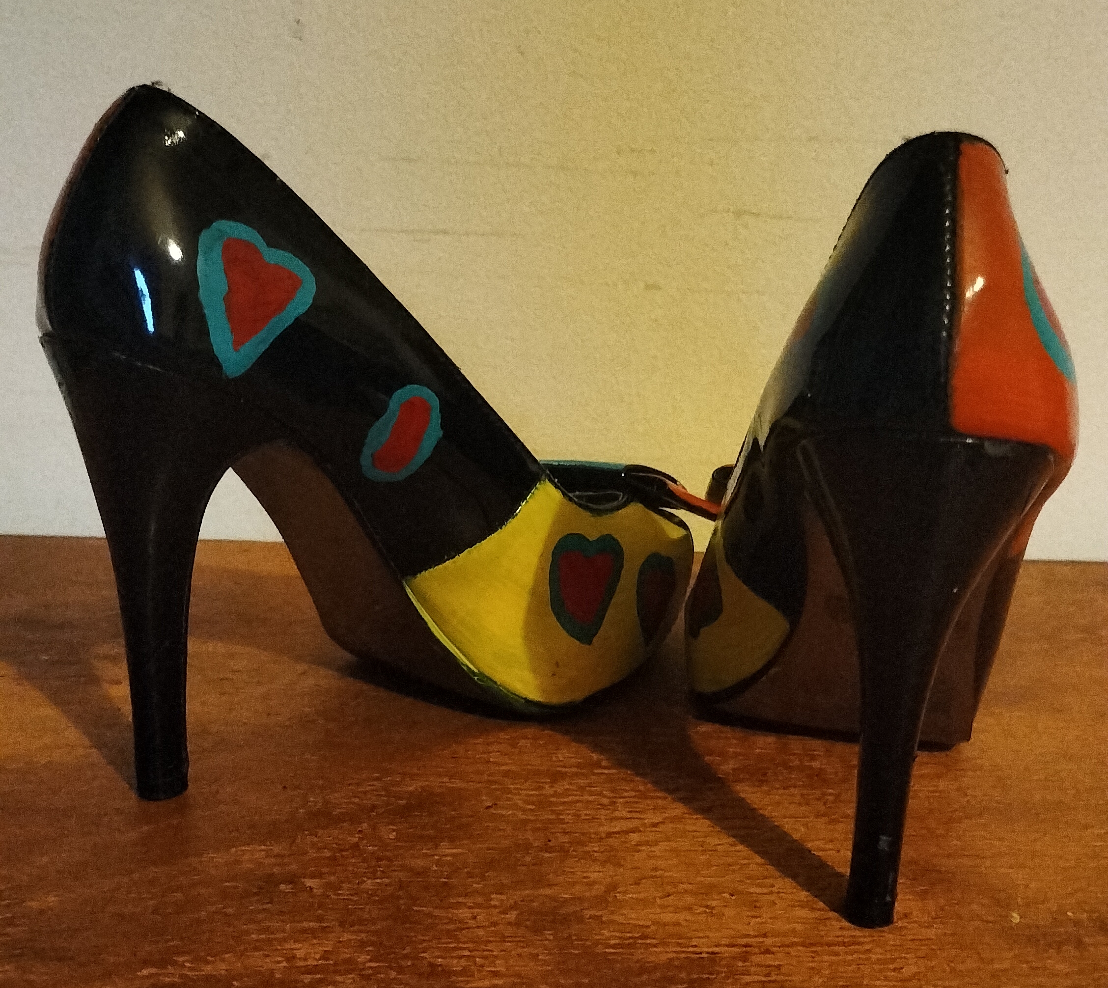 Size 3 or 4 peep toe shoes. Stiletto heels. Inside of shoes bottom half are painted yellow with red hearts surrounded in turquoise. Inside of upper part of the shoe is left plain apart from a couple of hearts in red with turquoise surround. Front of the shoes have bows. Hand painted too. Layered bows at the front and the lower layer is painted orangey/red with yellow spots and the top layer of the bow is turquoise with yellow spots. Outside of the shoe lower part is black shoe with hearts and the top half of the outside of the shoes are orange background with the red hearts surrounded in turquise. Small platform and open peep toe.