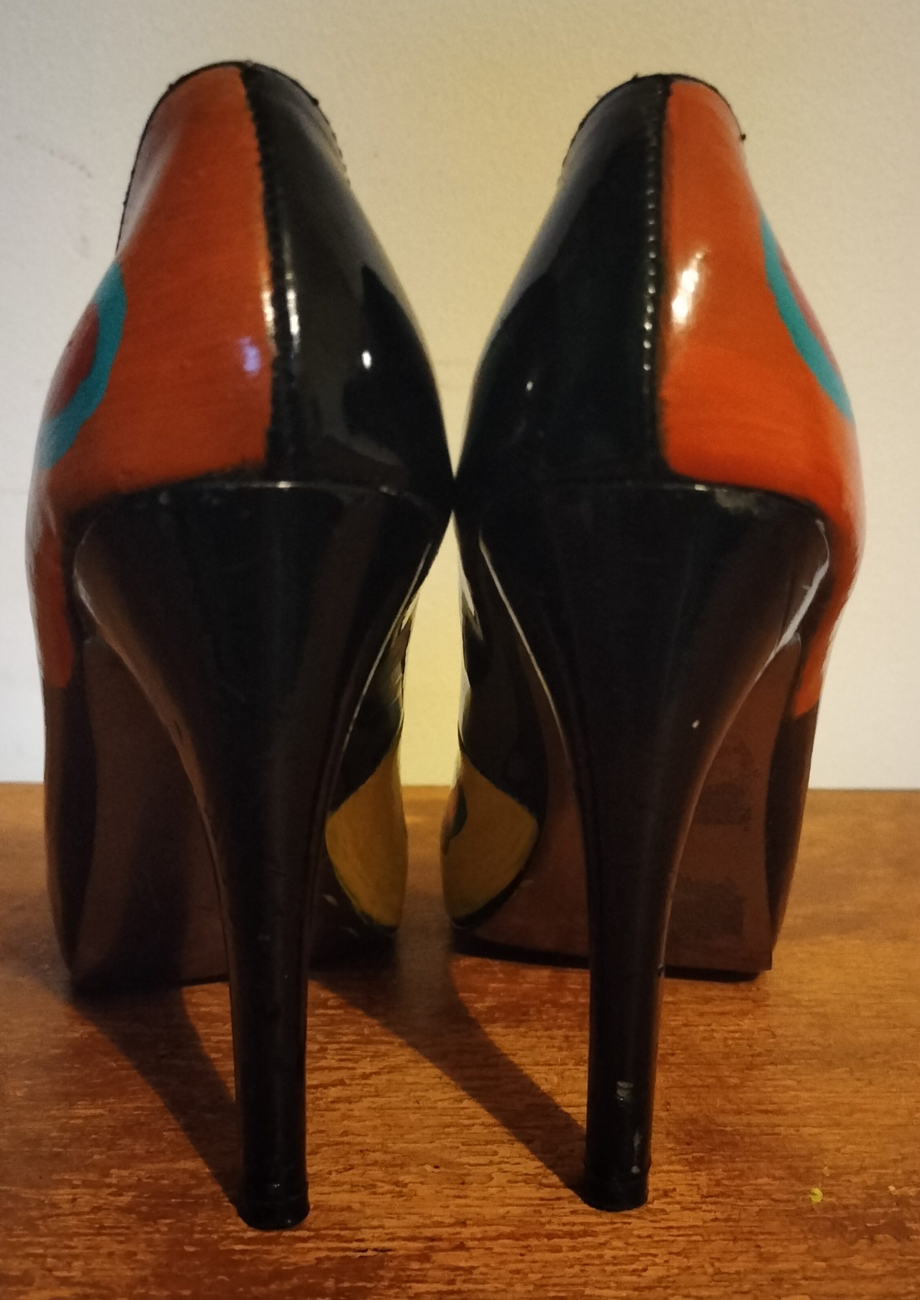 Size 3 or 4 peep toe shoes. Stiletto heels. Inside of shoes bottom half are painted yellow with red hearts surrounded in turquoise. Inside of upper part of the shoe is left plain apart from a couple of hearts in red with turquoise surround. Front of the shoes have bows. Hand painted too. Layered bows at the front and the lower layer is painted orangey/red with yellow spots and the top layer of the bow is turquoise with yellow spots. Outside of the shoe lower part is black shoe with hearts and the top half of the outside of the shoes are orange background with the red hearts surrounded in turquise. Small platform and open peep toe.