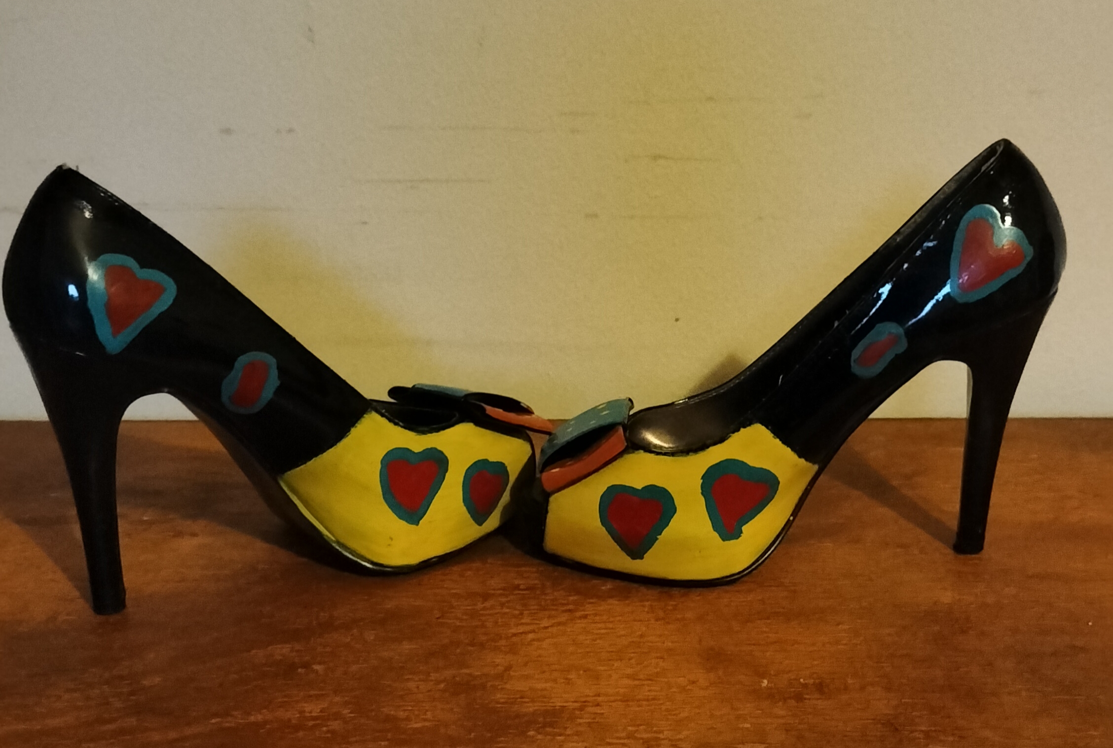 Size 3 or 4 peep toe shoes. Stiletto heels. Inside of shoes bottom half are painted yellow with red hearts surrounded in turquoise. Inside of upper part of the shoe is left plain apart from a couple of hearts in red with turquoise surround. Front of the shoes have bows. Hand painted too. Layered bows at the front and the lower layer is painted orangey/red with yellow spots and the top layer of the bow is turquoise with yellow spots. Outside of the shoe lower part is black shoe with hearts and the top half of the outside of the shoes are orange background with the red hearts surrounded in turquise. Small platform and open peep toe.