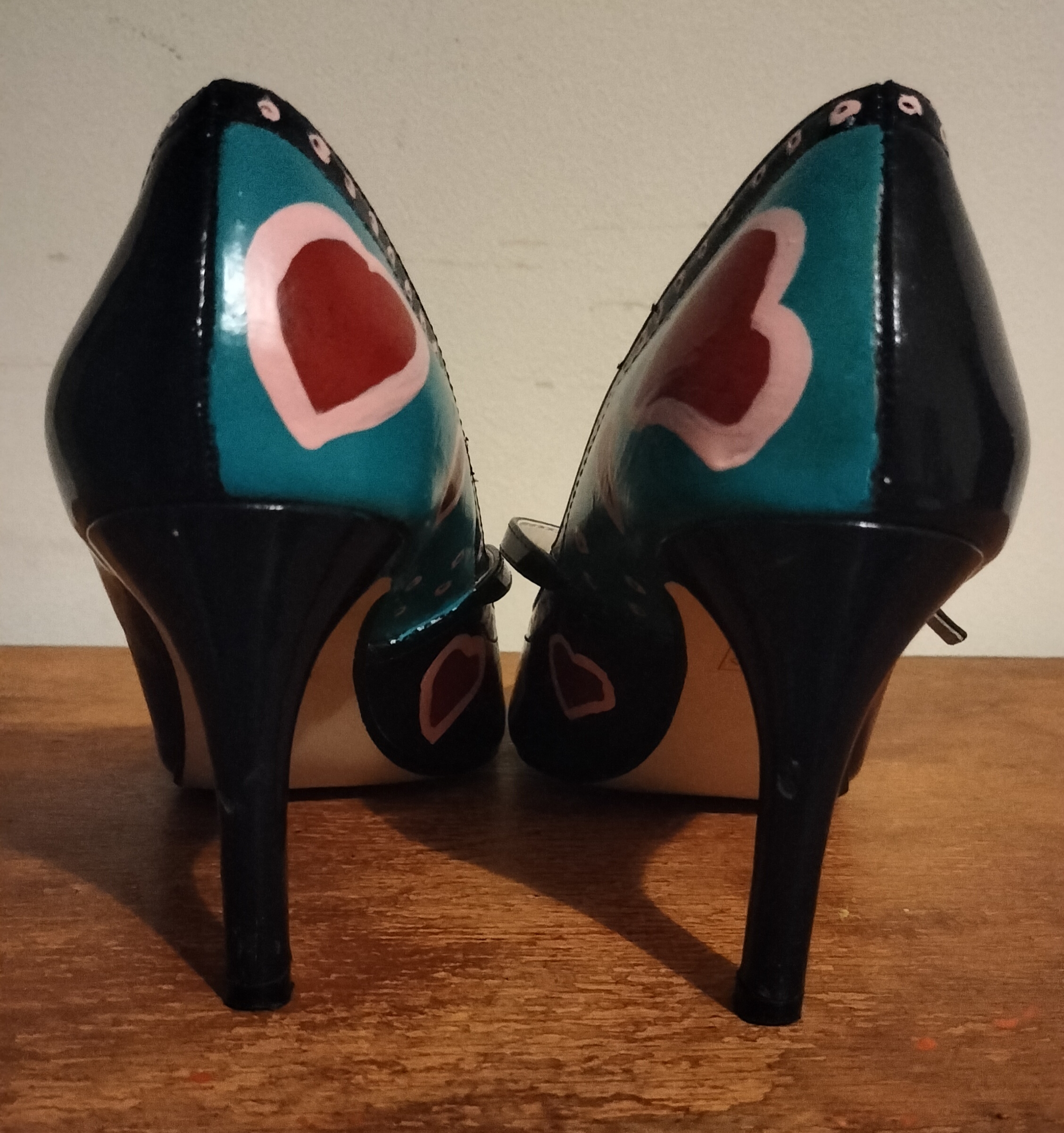 Size 5 hand painted navy blue The Collection shoes. Round toes and yellow spots and red and pink hearts on the front of the shoes. Thin strap across the front of your foot above the shoe. Stiletto heels. Pink little spots around the edge of the shoes at the front and around top of the side and back of the shoes. Heart shapes painted around the back of the shoes on the inside of the shoe. The outside of the shoe is left unpainted apart from the small pink spots that line the top of the shoe. Back of the heels on the insides painted turquoise with a heart on each of the shoes.