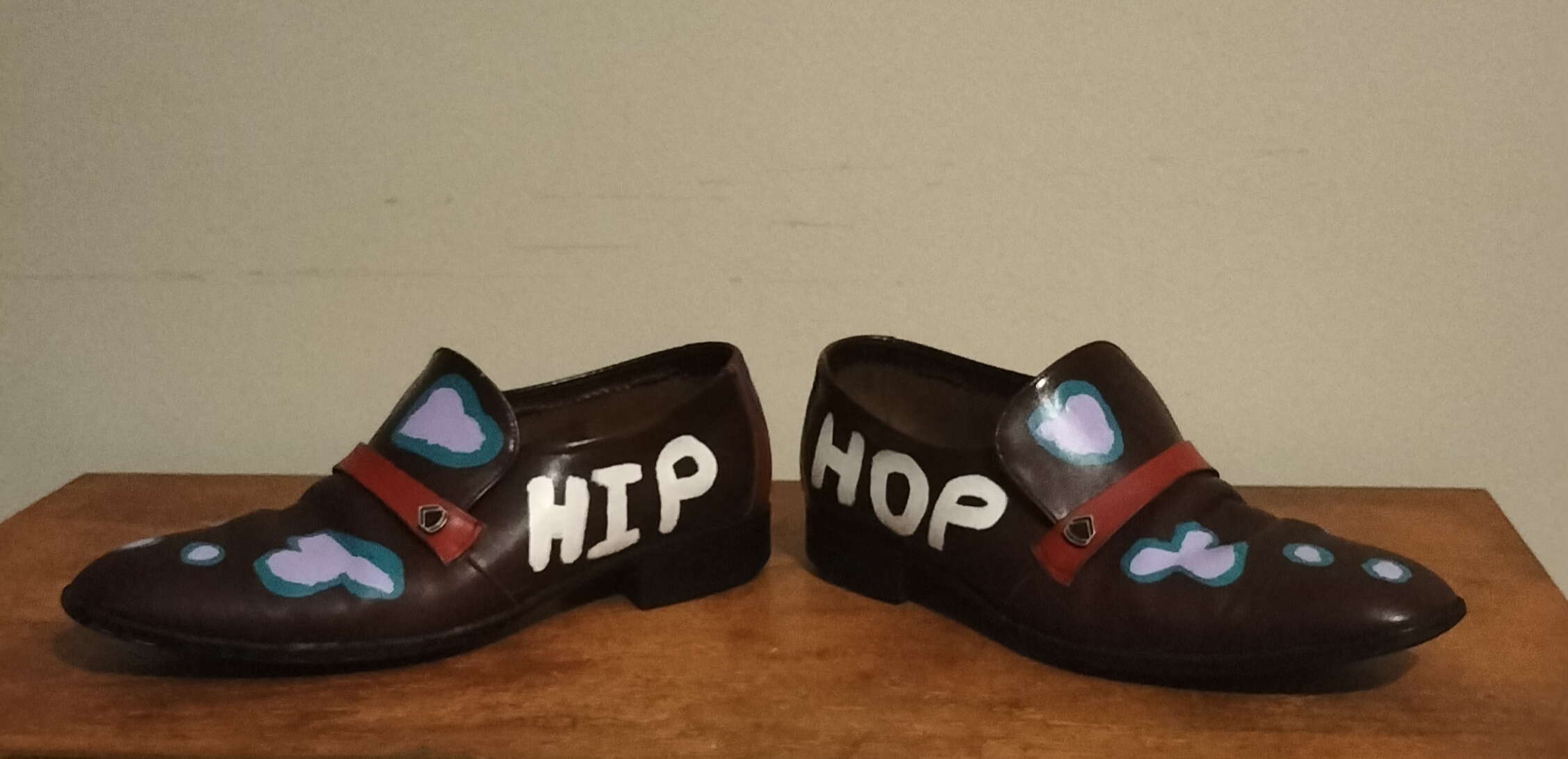 Size 7 hand painted brown leather shoes. The words Hip Hop across the shoes, hip on the side of one shoe and hop on the side of the other shoe. Front of shoes has leather strip which is painted red and there are lilac shapes surrounded with turquoise on both shoes. The back of the shoes are red with purple stripes. The inside of the shoes is like fine leaves and flowers. One offs.