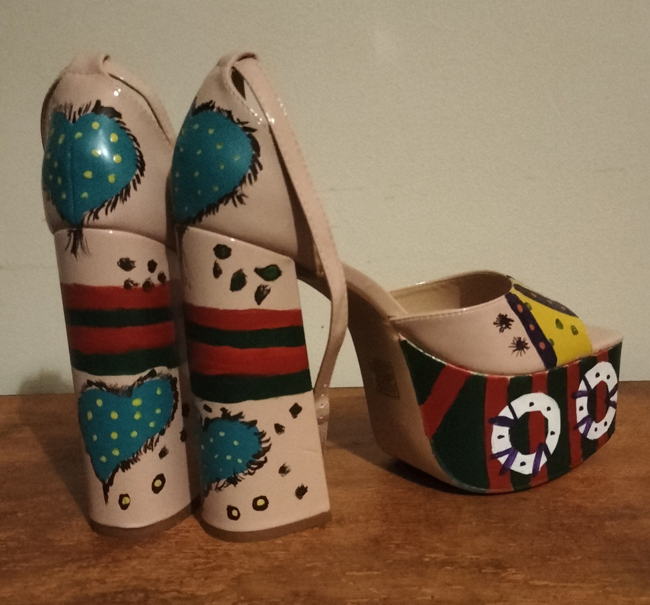 Size 8 preloved platform shoes. Beige uPVC handpainted. Proper funky and original. Green and red on the front platform (big) and then white circles with spots and lines. Turquoise hearts with yellow spots and black lines surrounding the hearts on the bottom of the heels and also on the back of the shoe behind your heel. Ankle straps. Open toe shoes. The section over the front of your foot is yellow and purple striped and there is more design on the side of the shoes. Original design.