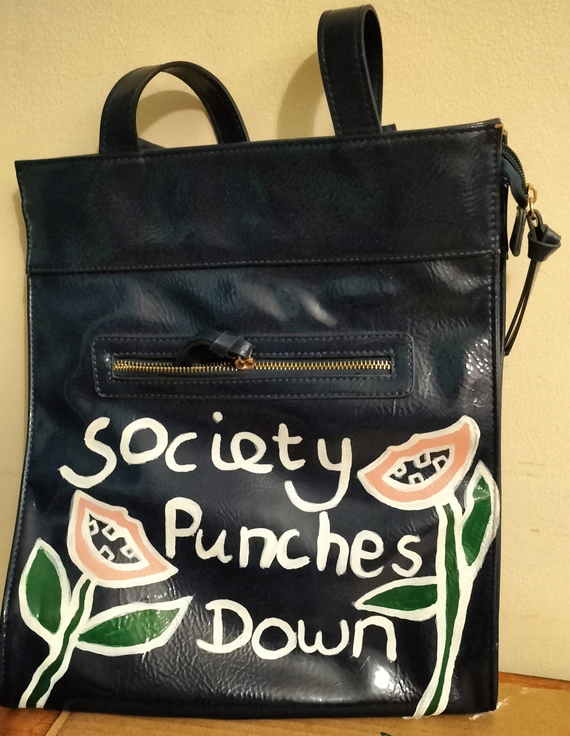 Hand painted handbag referencing the riots in Britain and how society punches down. People were called toothless amongst other things. Here's a couple of toothless flowers with the words Society Punches Down.