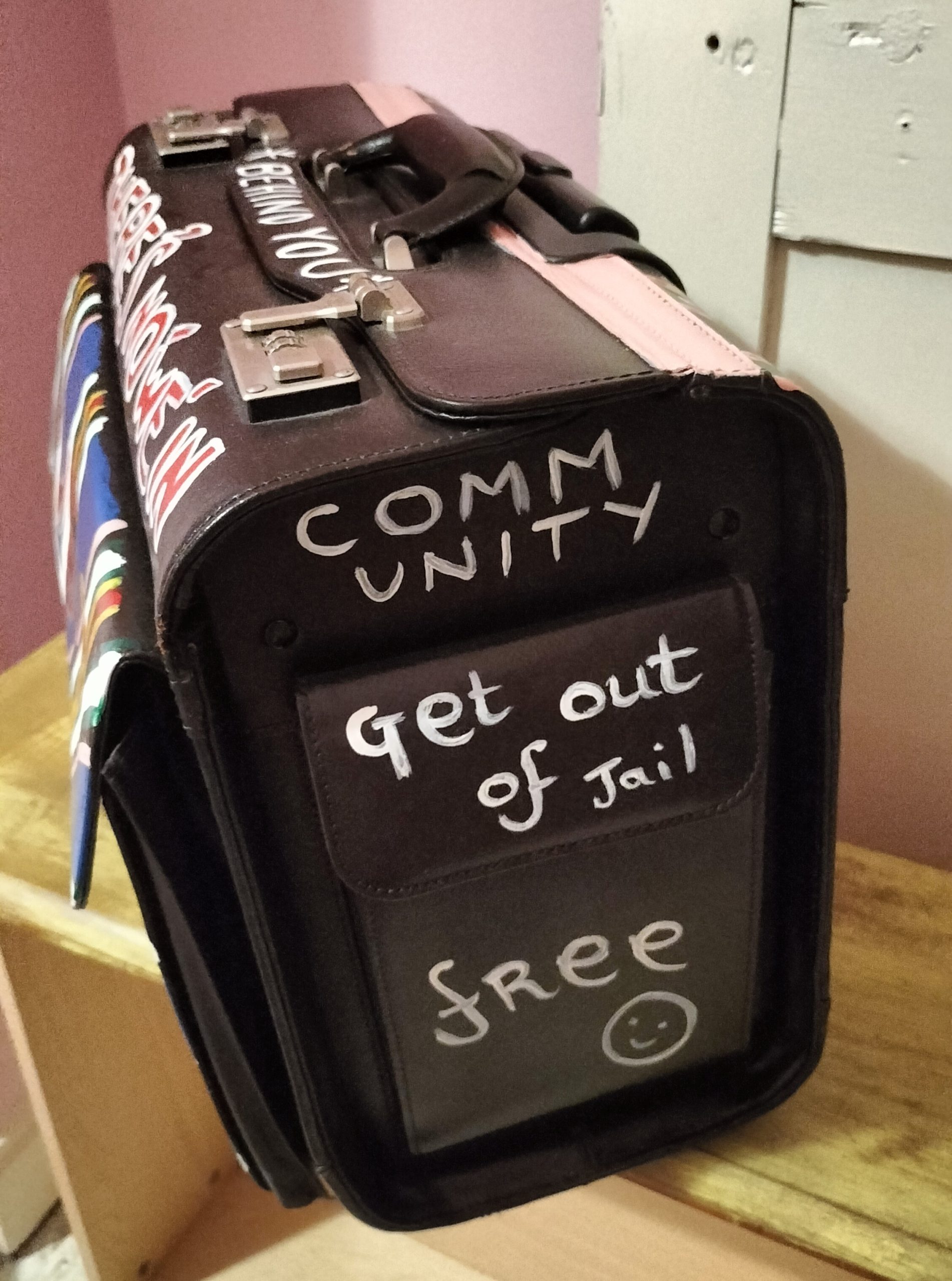 Hand painted side of pilot case saying Community and Get out of Jail Free with a smiling face. Referencing Monopoly the board game and part of a blog about identity, labelling, division and the elite. Talking about Britishness and Punch and Judy and finding out that an Italian man was involved in Punch and Judy.