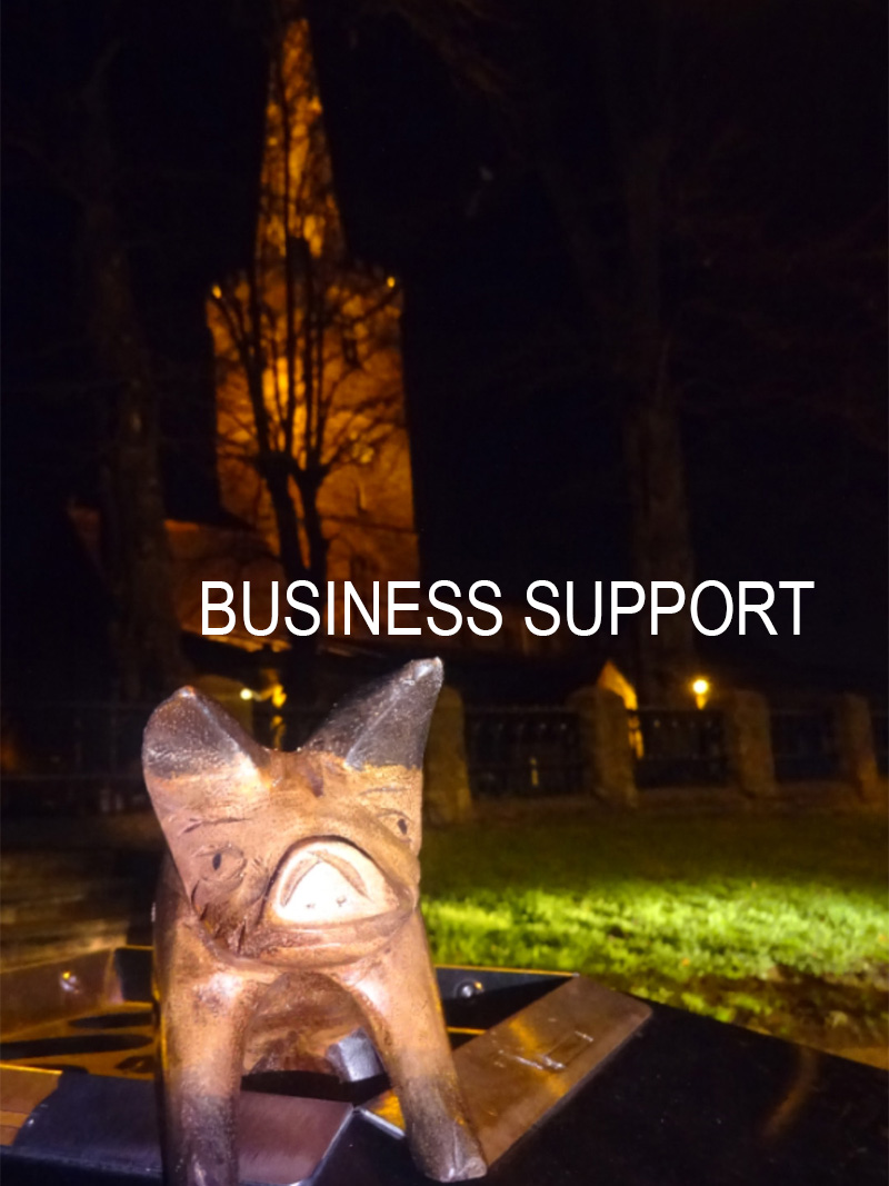 Services - business suport photograph of wooden pig ornament on street furniture in front of a church lit up in the darkness of the evening