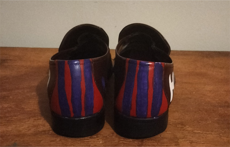 Back of shoes. Brown leather flat shoes. Back panel of shoes is painted red with purple vertical stripes.