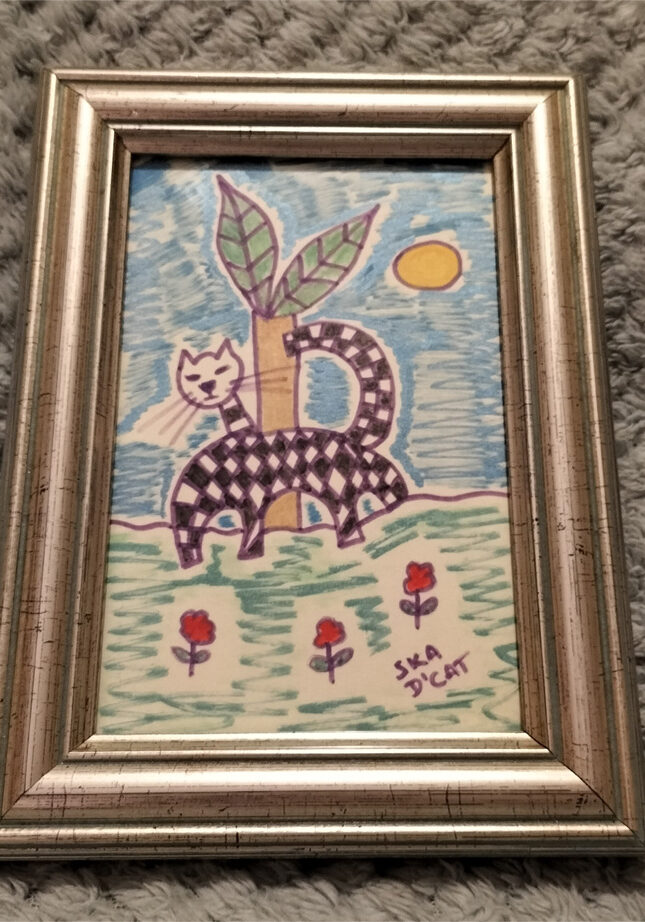 Ska d'cat little black and white cat, signature black and white squares associated with ska/two tone music. Small framed piece. Ska d'cat with flowers and blue and green background.