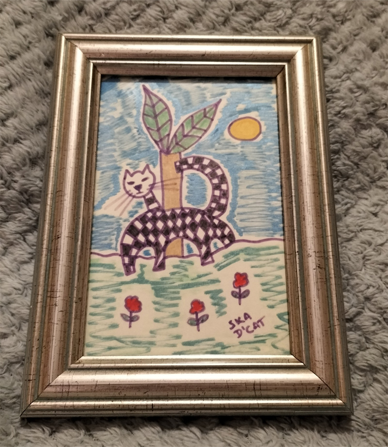Ska d'cat little black and white cat, signature black and white squares associated with ska/two tone music. Small framed piece. Ska d'cat with flowers and blue and green background.