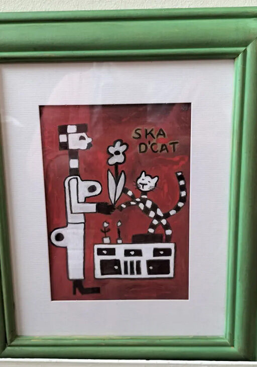 Ska d'cat original painting A4. Red background. Figure on the left holding a flower. Ska d'cat standing on a sideboard also holding the flower. Words read Ska d'cat. Black and white cat, signature black and white of ska/two tone music.