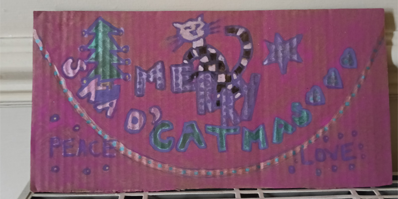 Ska d'cat Christmas design on cardboard. Pink background. Black and white cat. Reads Merry Ska c'catmas.