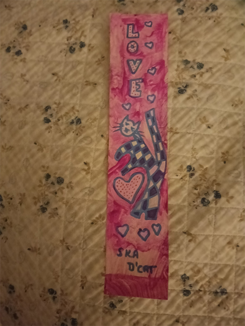 Tall bookmark or something to put on a shelf. Ska d'cat design with the word Love at the top. Tall, slim piece of card with pink paint background and hearts at the bottom of the image. Black and white ska d'cat.