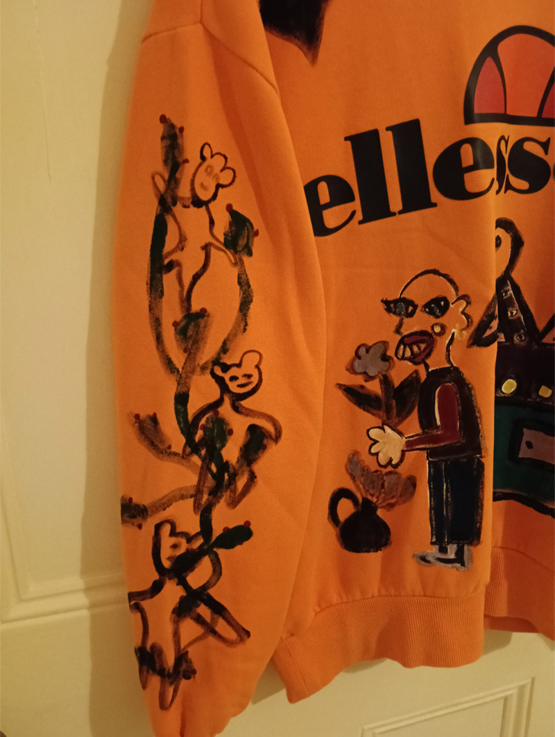 Ellesse orange size 16 sweatshirt. Hand painted front, back and sleeves. Front has illustration of abstract bird on sideboard alongside a figure holding a p;lant and flower and a little pot with flower coming out of it to the left. One sleeve has a vine-like design with monkeys in black outline paint and the other sleeve has black hearts on it. The back has the word "Brutal" and an abstract animal like a dog and a large boot with heel with squares looking like windows in a high rise flat. One off design.
