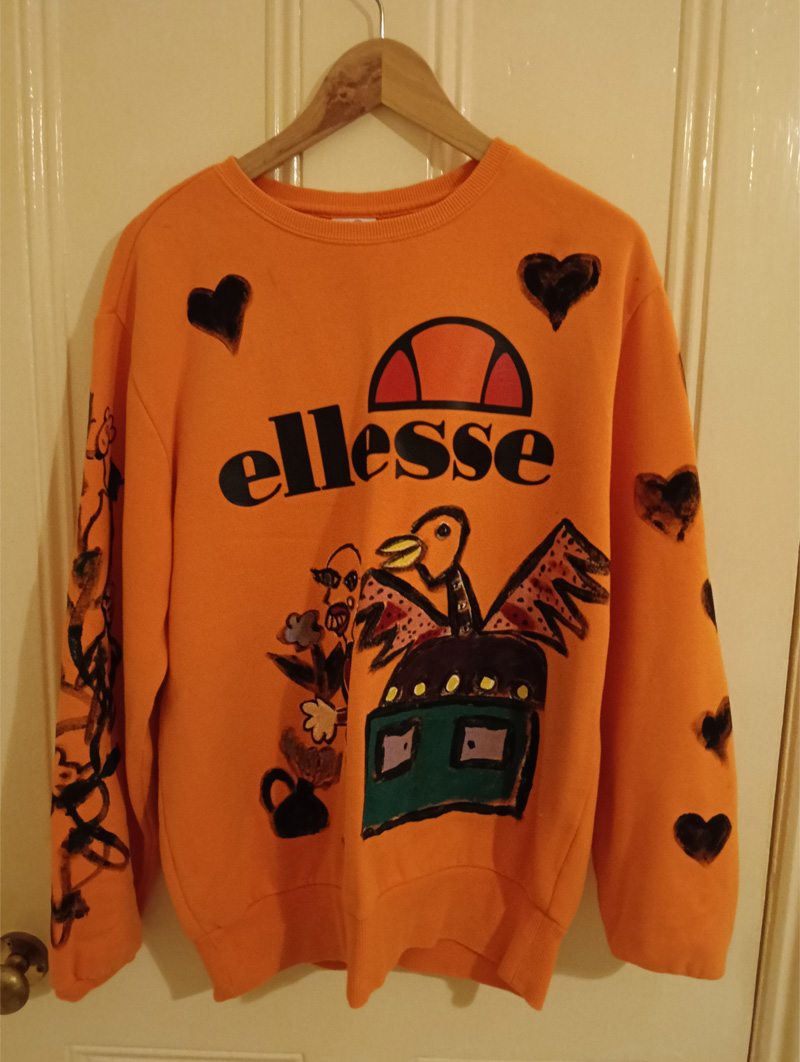 Ellesse orange size 16 sweatshirt. Hand painted front, back and sleeves. Front has illustration of abstract bird on sideboard alongside a figure holding a p;lant and flower and a little pot with flower coming out of it to the left. One sleeve has a vine-like design with monkeys in black outline paint and the other sleeve has black hearts on it. The back has the word "Brutal" and an abstract animal like a dog and a large boot with heel with squares looking like windows in a high rise flat. One off design.