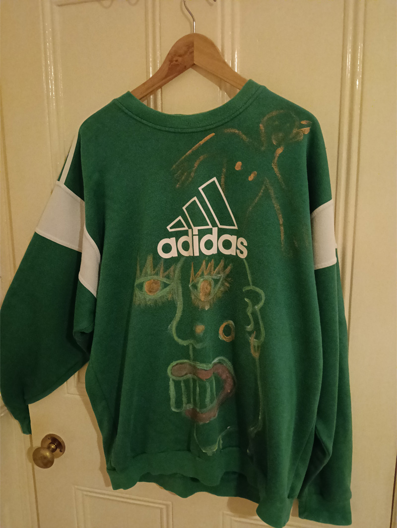 Green Adidas sweatshirt XL hand painted on the front. Back is not painted. On the front is a large figure head under the Adidas logo. Above the logo is a smaller figure. Original, one-off.