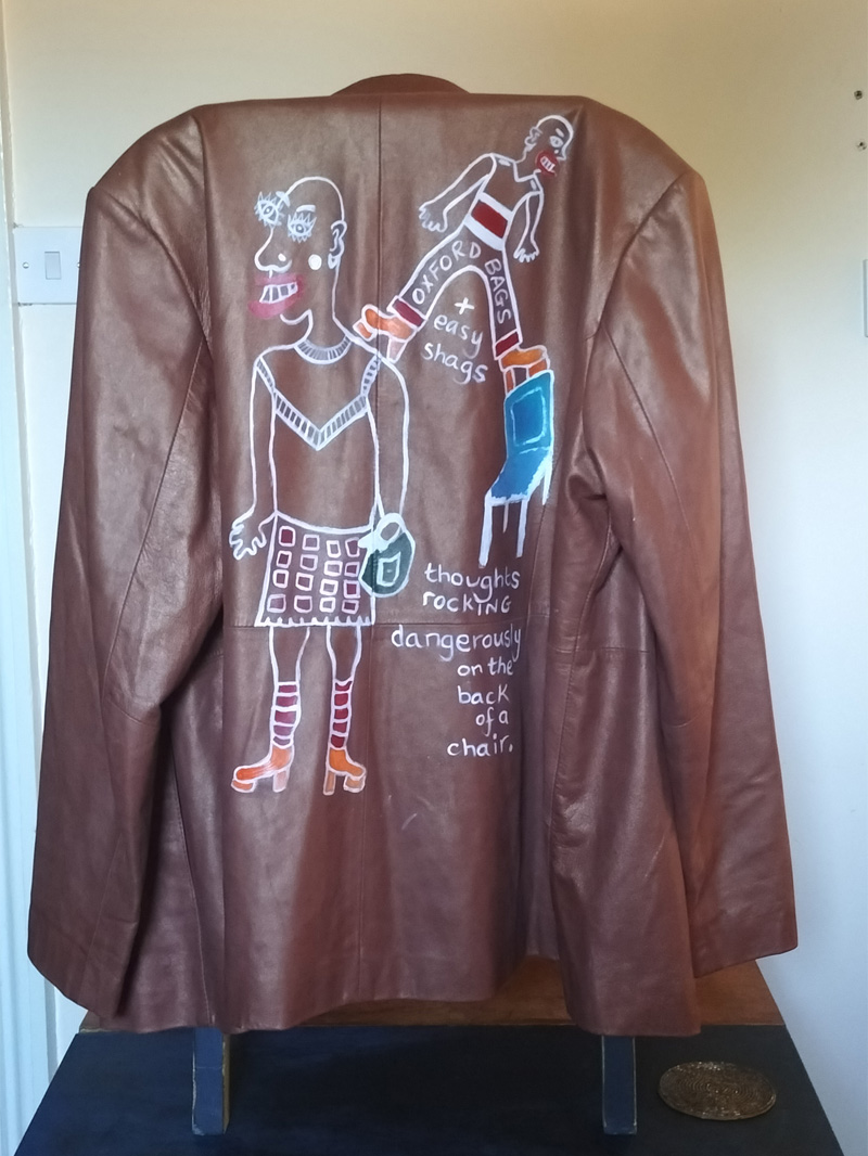 Back of jacket is hand painted. Figure on the left is wearing a skirt and top. Bald headed and carrying a handbag. Knee high socks and orange platform shoes. Smaller figure balancing on the main figure's shoulder and the top of a high backed chair. Similar shoes and trousers and top. Also bald headed. The words "Oxford Bags" across the trousers and between the legs below reads "+ easy shags". Blue chair. Words underneath the chair read "thoughts rocking dangerously on the back of a chair." Only painted on the back of the jacket. Buttoned up front. A slanted pocket to the left and right of the jacket. Arma leather jacket size 16. Brown.