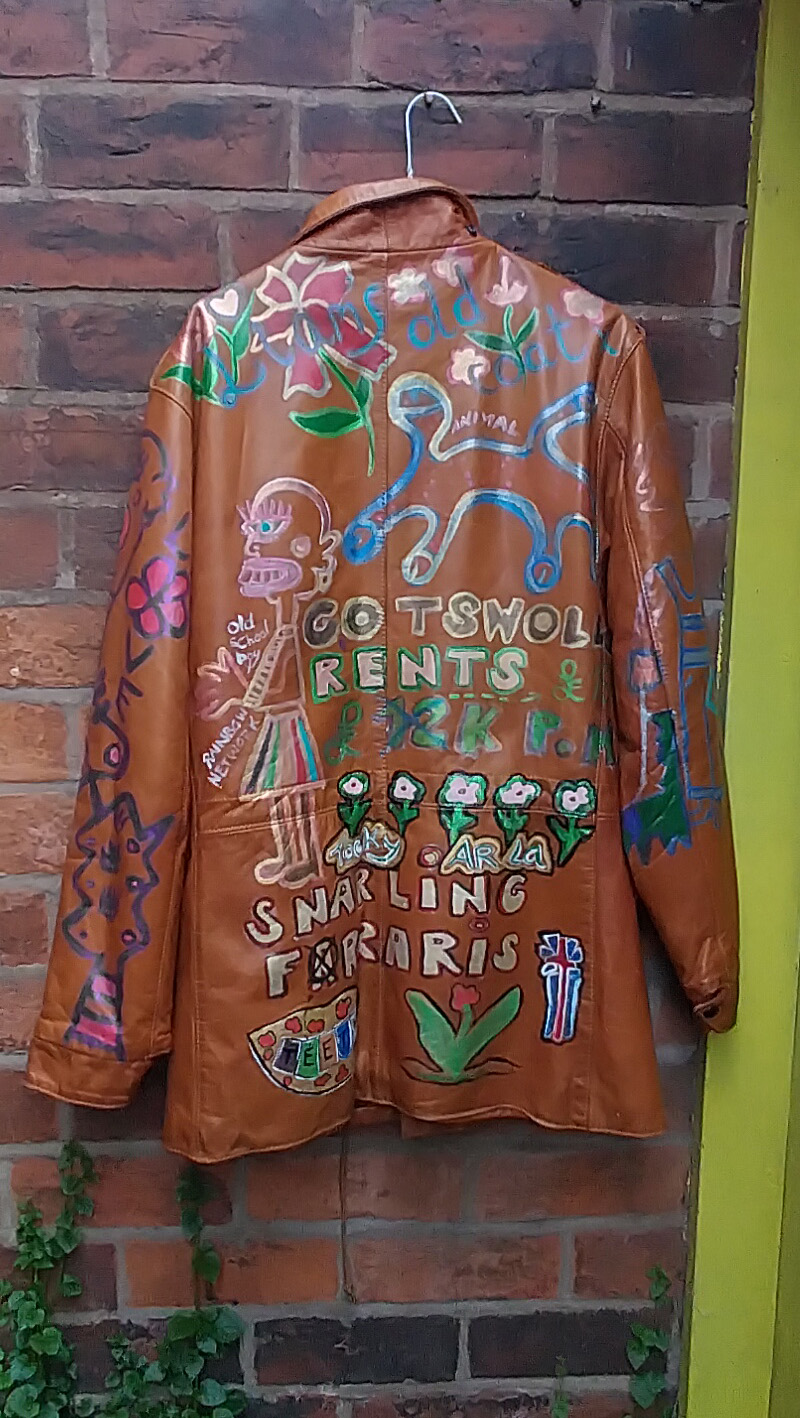 Liam's Old Coat - hand painted vintage parka jacket with hood (brown). Full image back of jacket hung against a wall in yard. Liam's Old Coat at the top of the jacket with flowers. Animal and abstract animal underneath. Character to the left of the area. Old School Boy. Rainbow Network. Figure in a skirt in different colours. Cotswolds Rents £12k pm crossed out with £19k pm. Tocky Ar La and flowers. Snarling Farraris (misspelt). Teeth and pointing one of the letters "e" to the word Farrari. A plant and an abstract British flag. Vintage Rome Peabody Massachusetts USA Size 42 brown leather hooded parka jacket handpainted one off.