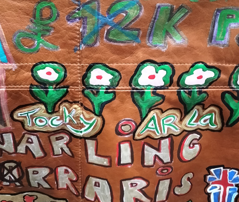 Liam's Old Coat - hand painted vintage parka jacket with hood (brown). Close up of lettering on the back of the jacket. Tocky Ar La (purposely misspelt) and row of flowers above the lettering. Below it other lettering and images. Vintage Rome Peabody Massachusetts USA Size 42 brown leather hooded parka jacket handpainted one off.