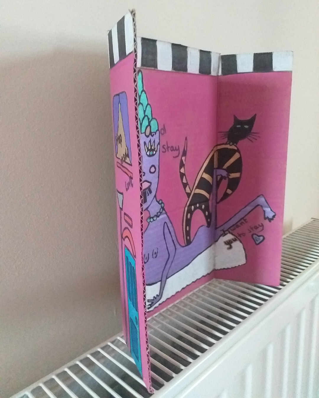 One for the lovers of Cilla Black piece uses some of the words of her song. Step inside love - and stay, I want you to stay cardboard art. About A4 landscape in size folded into three panels. When closed the front of the piece is like the front of a house. When opened it is a image of a purple woman on a rug with a cat and a plant. Front reads Step inside love. Inside reads and stay and lower down the image reads I want you to stay. The back of the image when opened out has painted parts on the left and right of the card and the centre piece is plain cardboard with a sticker on it. Step inside love on the front of the piece. Inside reads … and stay … I want you to stay.