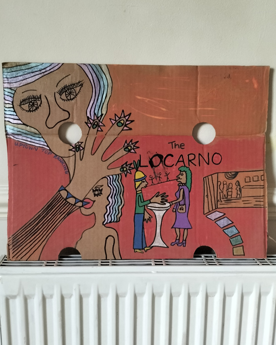 The Locarno cardboard art about A3 in size. The Locarno was a nightclub in Birmingham and there was Locarnos across England. This is a scene with a woman's face in top left of cardboard where a hole is her mouth and the words Uptown Top Ranking run under her hairline and around her chin and neck. The hand of the woman is coming up from the bottom left of the cardboard and the fingers are extended and look like chickens with spikey hair and a beak around each finger and the nail looks like an eyeball with eyelid (not detailed. There is the words The Locarno on the piece and a man and woman standing talking at a tall table. There is anoter woman under the hand where you only see part of her face. To the right of the image is a doorway and it looks like inside a room with slabs for stairway leading there. This is only small on the rigt side of the cardboard. Background is pink for the bottom two thirds of the cardboard and a kind of orage for the top third of the card.The Locarno cardboard art about A3 in size. The Locarno was a nightclub in Birmingham and there were Locarno nightclubs across England. This is a scene with a woman's face in top left of cardboard where a hole is her mouth and the words Uptown Top Ranking run under her hairline and around her chin and neck. The hand of the woman is coming up from the bottom left of the cardboard and the fingers are extended and look like chickens with spikey hair and a beak around each finger and the nail looks like an eyeball with eyelid (not detailed). There is the words The Locarno on the piece and a man and woman standing talking at a tall table. There is another woman under the hand where you only see part of her face. To the right of the image is a doorway and it looks like inside a room with slabs for stairway leading there. This is only small on the right side of the cardboard. Background is pink for the bottom two thirds of the cardboard and a kind of orange for the top third of the card.