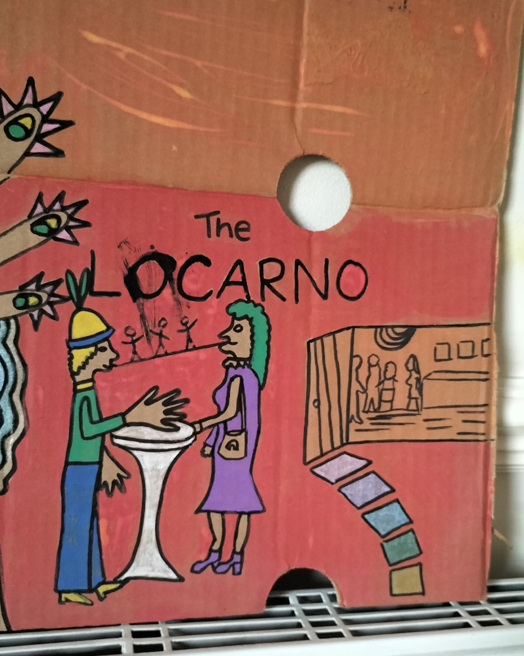 Bottom right of art work. The Locarno cardboard art about A3 in size. The Locarno was a nightclub in Birmingham and there were Locarno nightclubs across England. This is a scene with a woman's face in top left of cardboard where a hole is her mouth and the words Uptown Top Ranking run under her hairline and around her chin and neck. The hand of the woman is coming up from the bottom left of the cardboard and the fingers are extended and look like chickens with spikey hair and a beak around each finger and the nail looks like an eyeball with eyelid (not detailed). There is the words The Locarno on the piece and a man and woman standing talking at a tall table. There is another woman under the hand where you only see part of her face. To the right of the image is a doorway and it looks like inside a room with slabs for stairway leading there. This is only small on the right side of the cardboard. Background is pink for the bottom two thirds of the cardboard and a kind of orange for the top third of the card.
