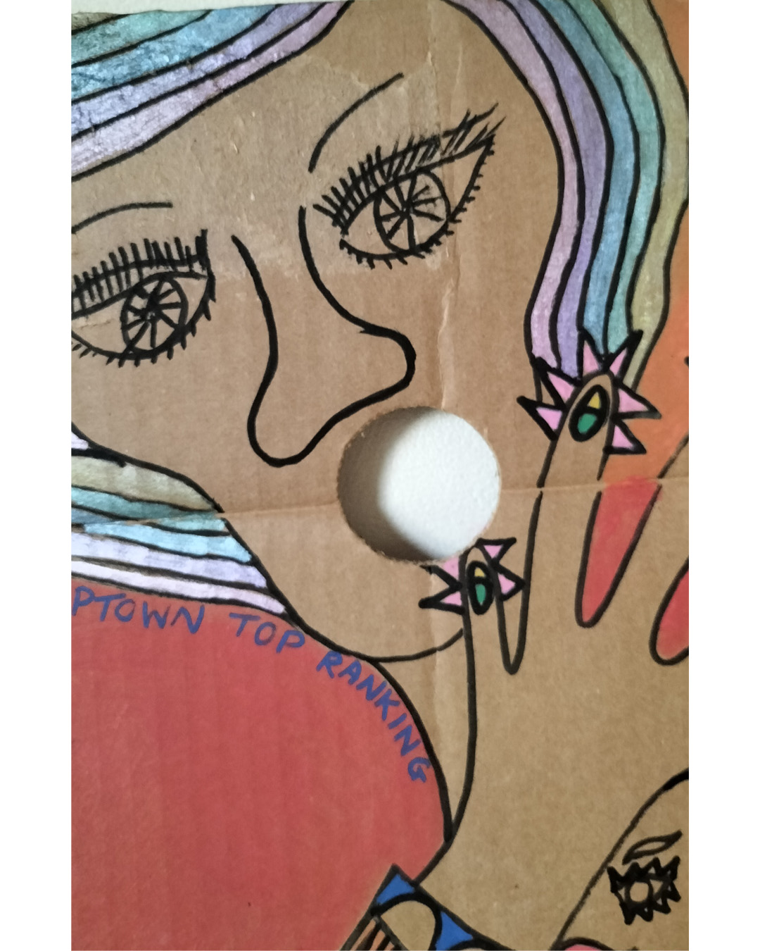 Close up of face at top left. The Locarno cardboard art about A3 in size. The Locarno was a nightclub in Birmingham and there were Locarno nightclubs across England. This is a scene with a woman's face in top left of cardboard where a hole is her mouth and the words Uptown Top Ranking run under her hairline and around her chin and neck. The hand of the woman is coming up from the bottom left of the cardboard and the fingers are extended and look like chickens with spikey hair and a beak around each finger and the nail looks like an eyeball with eyelid (not detailed). There is the words The Locarno on the piece and a man and woman standing talking at a tall table. There is another woman under the hand where you only see part of her face. To the right of the image is a doorway and it looks like inside a room with slabs for stairway leading there. This is only small on the right side of the cardboard. Background is pink for the bottom two thirds of the cardboard and a kind of orange for the top third of the card.